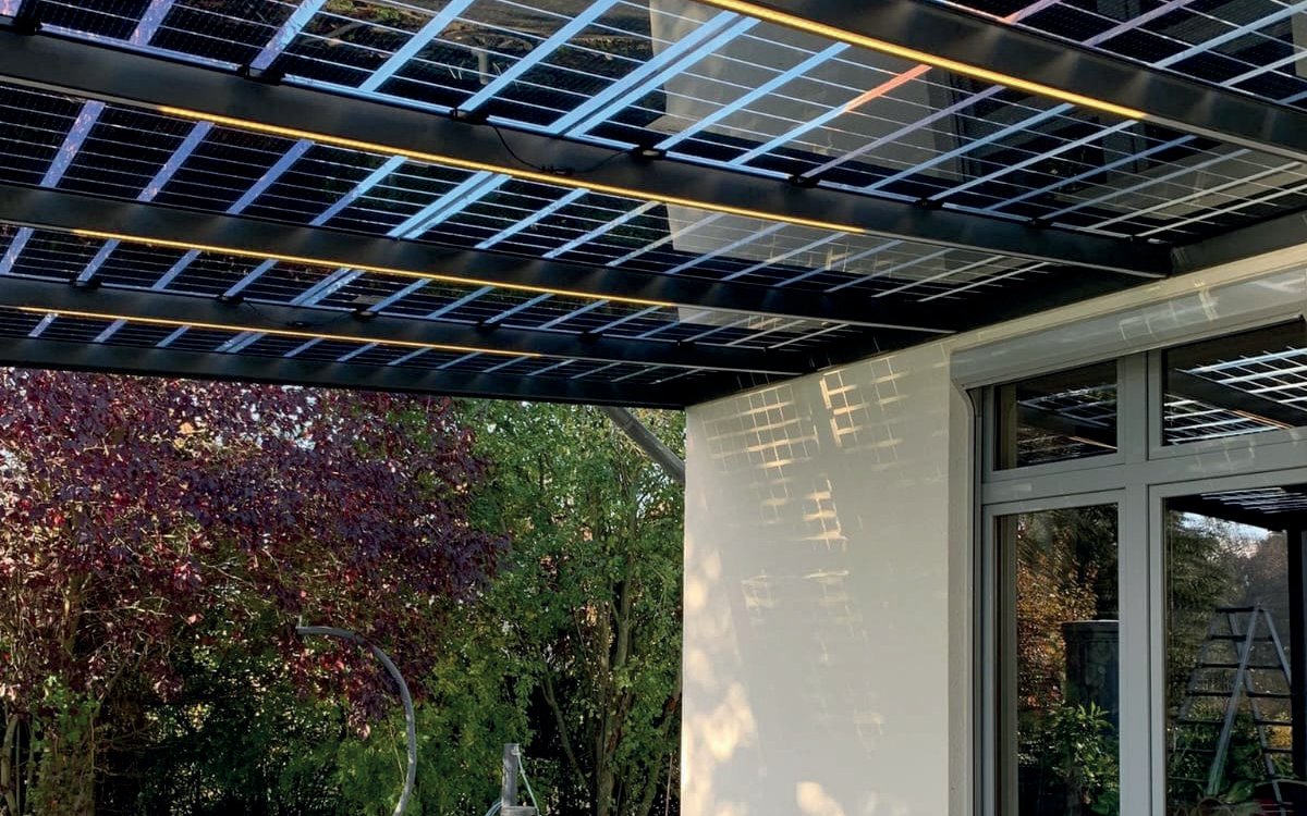 Untersicht einer Solarterrasse im Abendlicht: Sonne fällt zwischen den semitransparenten Modulen hindurch auf die Hauswand